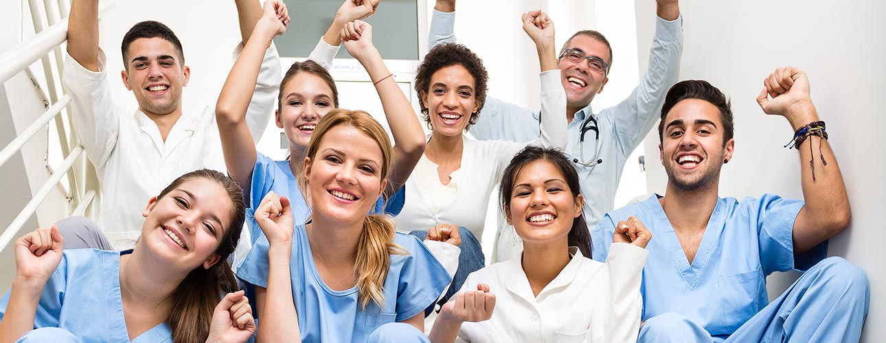 Ein Team aus Männern und Frauen in Pflegeuniform lächelt und macht eine kraftvolle Geste mit der Hand.