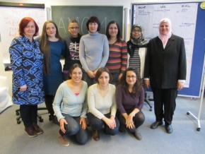 Eine Gruppe von Frauen steht vor zwei Tafeln. Drei von ihnen hocken vor den dahinter stehenden Frauen.