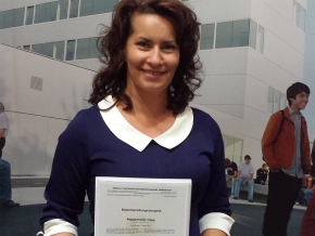 Irina Mayerhofer lächelt und hält stolz ihr Diplomprüfungszeugnis in die Kamera