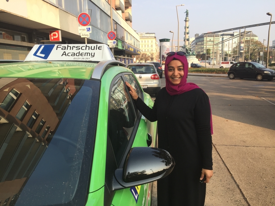 Zekiye Cantilav steht neben dem Fahrschulauto und lächelt in die Kamera.