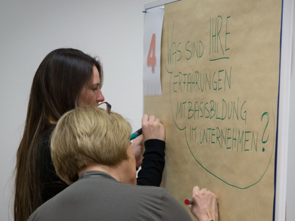 Zwei Frauen schreiben auf ein Flipchart zum Thema "Was sind ihre Erfahrungen mit Basisbildung im Unternehmen?"