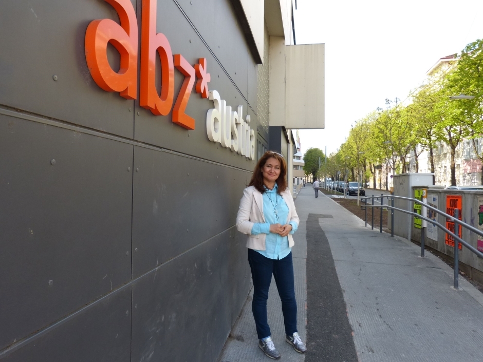 Eine Frau mit dunkelbraunen Haaren steht vor dem ABZ*AUSTRIA Gebäude und lächelt in die Kamera.