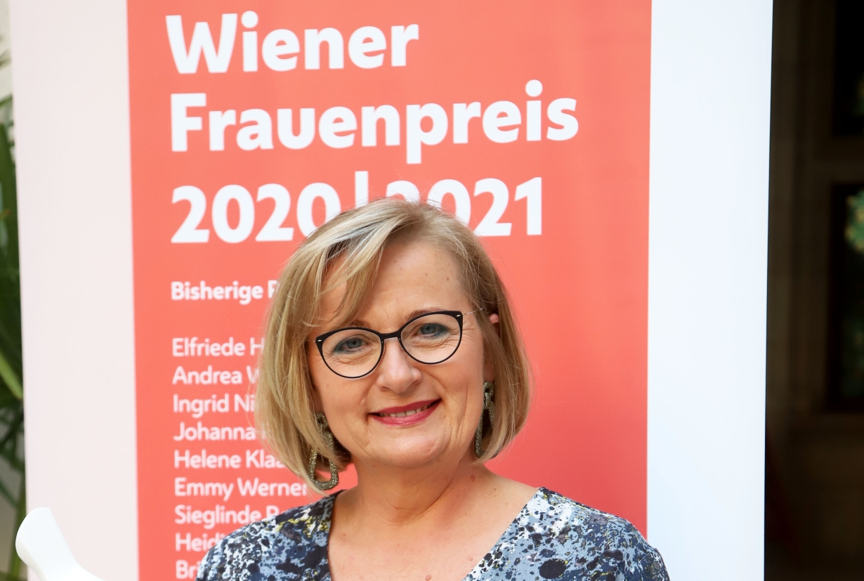 Manuela Vollmann vor einem Plakat mit der Aufschrift "Wiener Frauenpreis 2021"