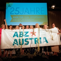 Mitarbeiterinnen halten ein großes Plakat auf der Bühne mit der Aufschrift ABZ*AUSTRIA, ABZ*AUSTRIA 25 Jahre ABZ*AUSTRIA