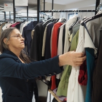 Dame betrachtet die Kleidungsstücke in den Hängeregalen. ABZ*AUSTRIA ABZ*Business Second Hand Markt