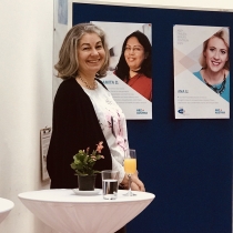 Lächelnde Dame steht vor einer Pinwand mit Plakaten. ABZ*AUSTRIA Fünf Jahre ABZ*Frauenberufszentrum Wien