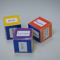Drei bunte Würfel aus Papier mit der Aufschrift "keck", "Kompetenz" und "lernen"