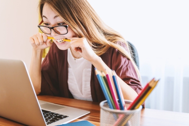 Eine Frau mit Brille beißt gestresst auf einen Bleistift. Vor ihr steht ein offener Laptop.