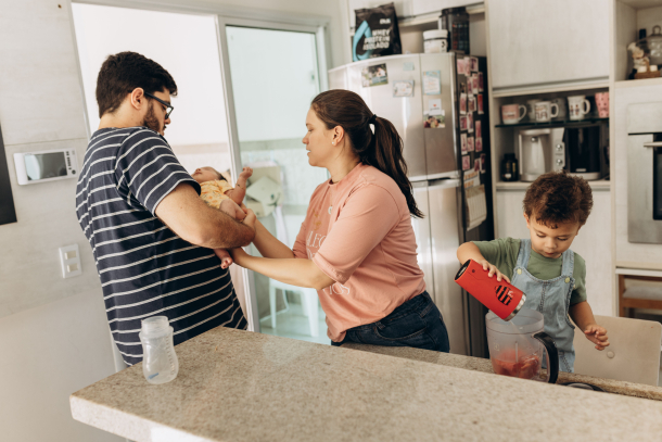 Vater hält Baby und steht mit Frau und zweitem Kind in der Küche